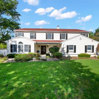 A two-story suburban house with a well-maintained lawn and trees under a blue sky.