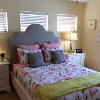 A cozy bedroom featuring a bed with floral bedding and multiple pillows, flanked by nightstands with lamps.