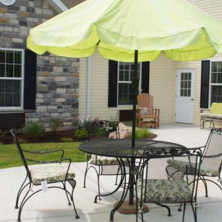 A cozy backyard patio with a table, chairs, and a green umbrella.