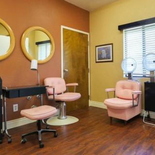 A vintage-style hair salon interior featuring pink chairs and round mirrors against a warm color palette.