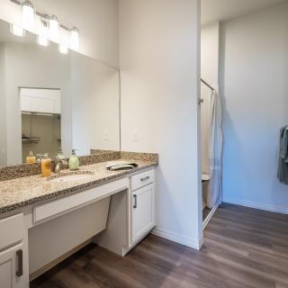 A modern bathroom with a vanity, mirror, and shower area.