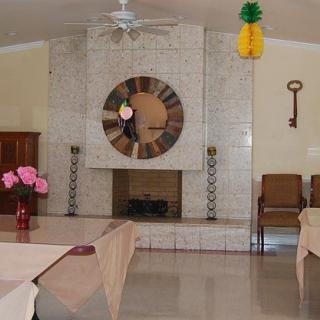 A cozy dining room with a large clock above the fireplace and tables set with pink flowers.
