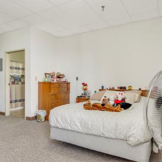 A cozy bedroom with a bed adorned with stuffed animals and a wooden dresser nearby.