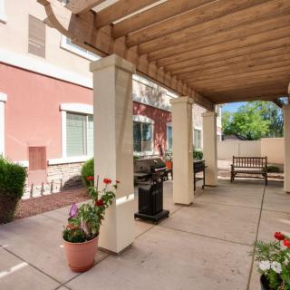 A cozy outdoor patio with a pergola, featuring potted flowers, a bench, and a grill.