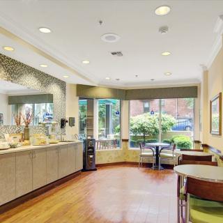 A cozy cafe interior with a beverage station and seating, featuring modern decor and large windows.
