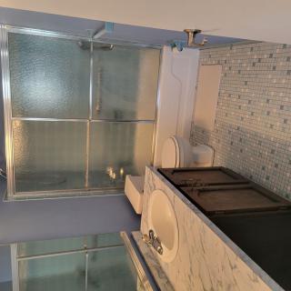 A modern bathroom with a marble countertop, glass shower doors, and tiled flooring.