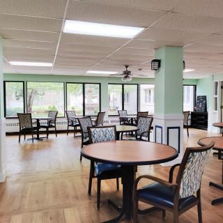 A spacious dining area with several tables and chairs, featuring large windows allowing natural light.