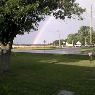 A beautiful rainbow arches over a serene landscape, with lush green grass and trees.