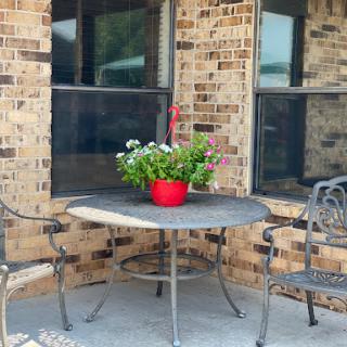 A cozy outdoor seating area featuring a table, chairs, and a vibrant flower arrangement in a red pot.