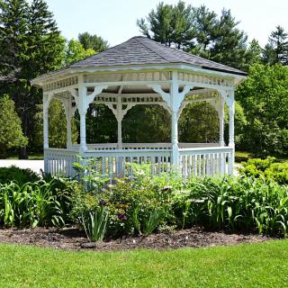 A white gazebo surrounded by lush greenery in a garden setting.