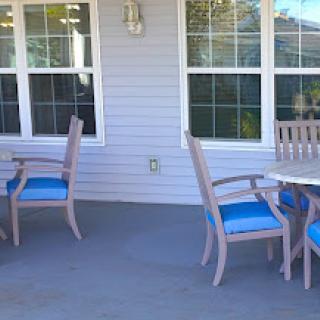 A cozy outdoor patio area featuring wooden chairs with blue cushions and a couple of tables, perfect for relaxation.