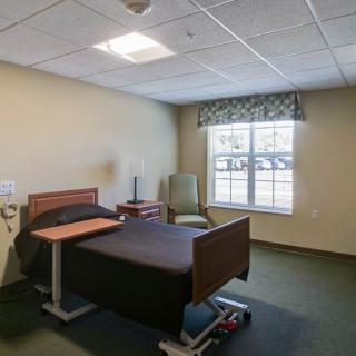 A hospital room with a single bed, chair, and window.