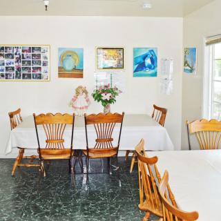 A cozy dining area with wooden chairs and tables, decorated with artwork and a flower arrangement.