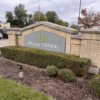 A brick sign marked with 'Bella Terra' surrounded by bushes and greenery.