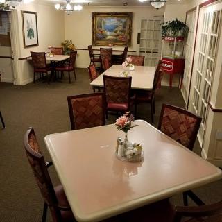 A well-lit dining area with multiple tables and chairs, adorned with paintings and plants, creating a cozy atmosphere.