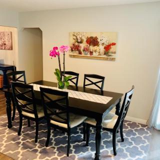 A well-decorated dining area featuring a dark wood table with matching chairs, adorned by vibrant orchids and complemented by wall art and a patterned carpet.