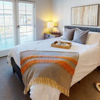 A cozy bedroom with a neatly made bed, a colorful throw blanket, and soft lighting from a table lamp.