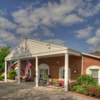 A welcoming entrance to a building adorned with flags and surrounded by lush landscaping under a partly cloudy sky.