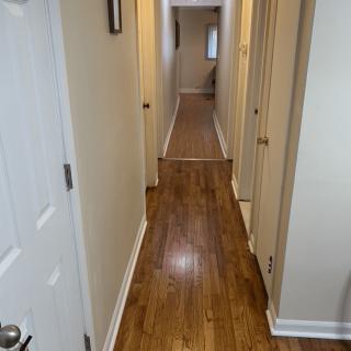 A long hallway with wooden flooring and several doors on each side.