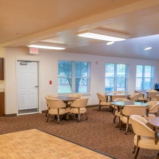 A spacious dining area with multiple tables and chairs, featuring large windows and comfortable lighting.