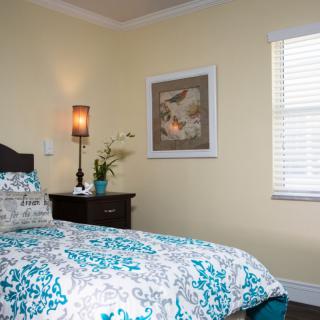 A cozy bedroom with a floral-patterned bedspread, a bedside table with a lamp and plant, and wall artwork.