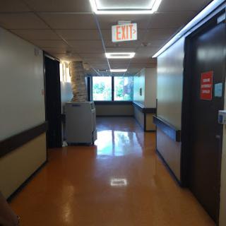 A well-lit hospital hallway with windows, showing the orange flooring typical of medical facilities.