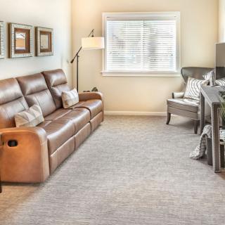 A cozy living room with a brown leather sofa, armchair, and a large window.