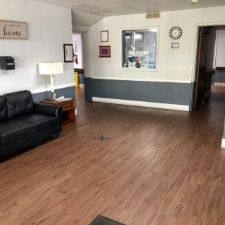 A cozy waiting room with a black sofa, wooden flooring, and wall decor.
