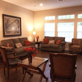 A cozy living room with sofas and armchairs arranged around a central table, warm lighting, and decorative elements.