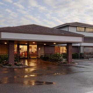A welcoming entrance of a building during twilight, reflecting the soft glow of interior lights on the wet pavement.