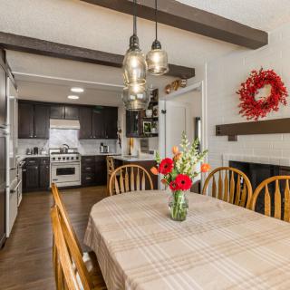 A cozy kitchen-dining area with a wooden table, adorned with flowers and illuminated by pendant lights.
