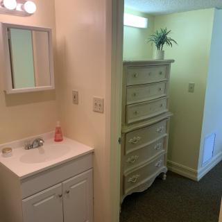 A small bathroom area with a sink, mirror, and dresser in a cozy interior setting.