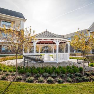 A charming gazebo surrounded by well-maintained gardens and greenery, with a bench positioned in front.