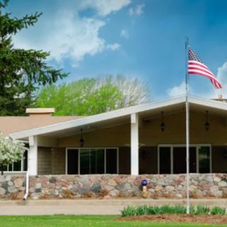 A building with an American flag in front, surrounded by trees and under a partly cloudy sky.