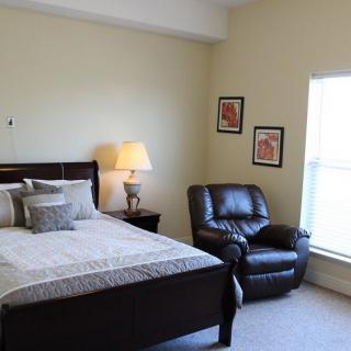 A cozy bedroom with a bed, armchair, and lamp beside a window.