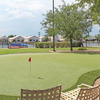 A serene golf putting green overlooking a lake with benches and nearby residential homes.