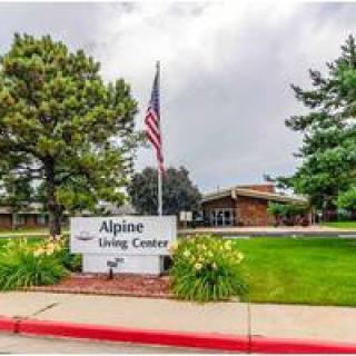 A view of the Alpine Living Center with a sign and an American flag in front of the building.
