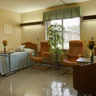 A hospital room with a bed, chairs, and a window.