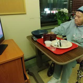 An elderly person enjoying a meal while watching television in a care facility.