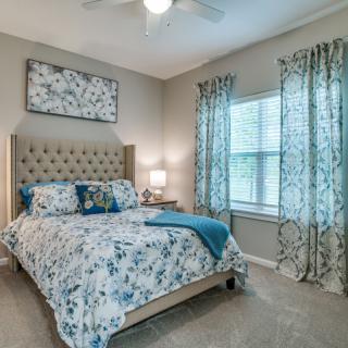 A cozy bedroom with floral bedding and matching curtains, featuring a lamp on the bedside table.