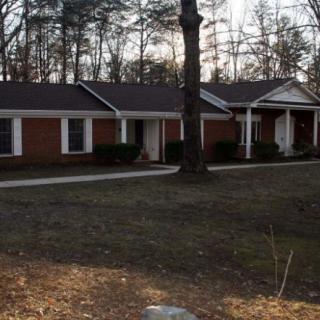 A suburban single-story brick house with trees and a yard.