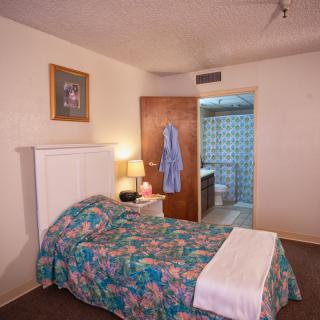 A cozy bedroom with a colorful bedspread, nightstand, and a view into the bathroom.