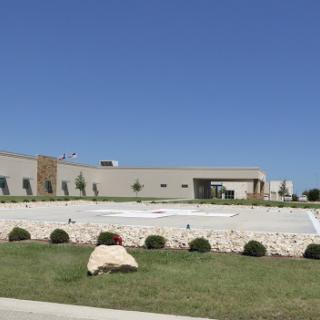 A modern commercial building set against a clear blue sky, featuring landscaped grounds and a spacious parking area.