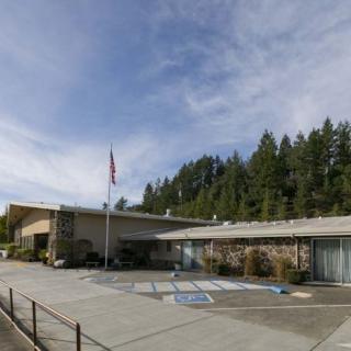 A hospital building with a parking lot, surrounded by trees and under a cloudy sky.