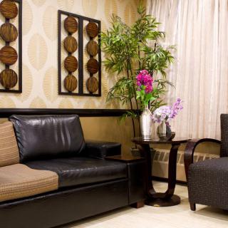 A cozy living room with modern furniture, featuring a dark sofa, an armchair, a coffee table with floral arrangements, and artistic wall decor.