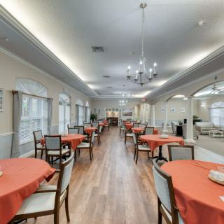 A spacious dining room with neatly arranged tables covered in orange tablecloths and elegant chandeliers hanging from the ceiling.
