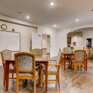 A well-lit dining area with wooden flooring and multiple tables and chairs.