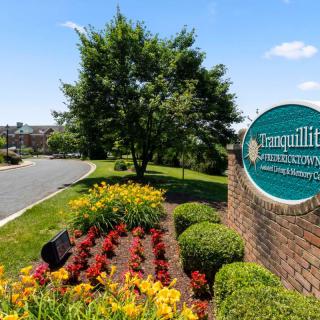 A landscaped entrance with a sign, colorful flowers, and a tree under a clear blue sky.