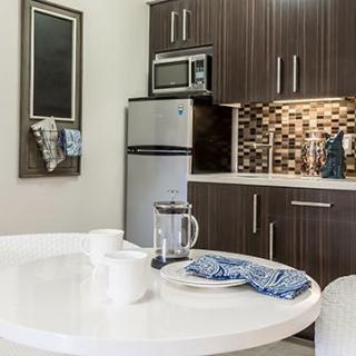 A modern kitchen with sleek cabinets, a stainless steel fridge and microwave, and a round white dining table set for two.