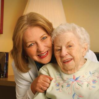 An elderly woman smiling with a caregiver indoors.